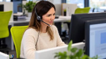 Operatrice di Itacall Group con cuffie al computer, in una scena illustrativa del contatto telefonico con una pubblica amministrazione